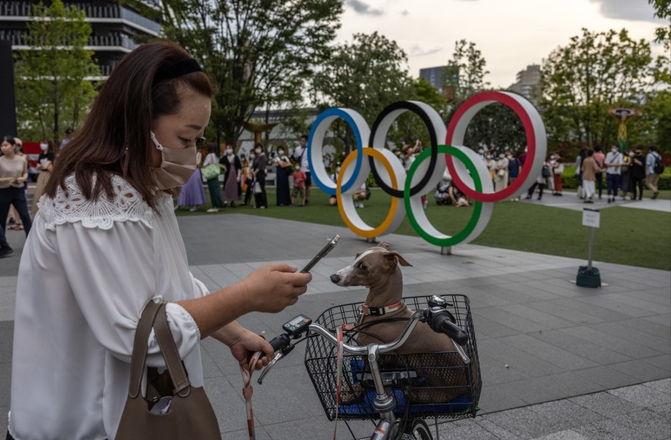 A woman in her mask next to the Olympic rings in downtown Tokyo