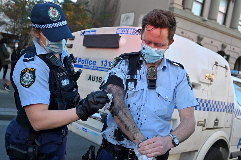 A police officer wipes away the paint thrown by a protester on her colleague in Sydney