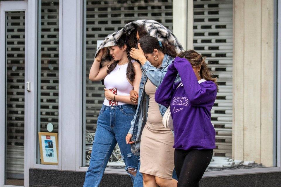 Three friends shelter their faces from the wind and rain in Preston, Lancashire