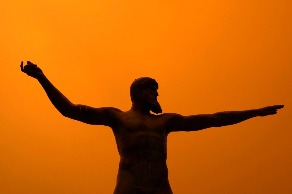 The sky turned red from the flames behind a statue of Poseidon