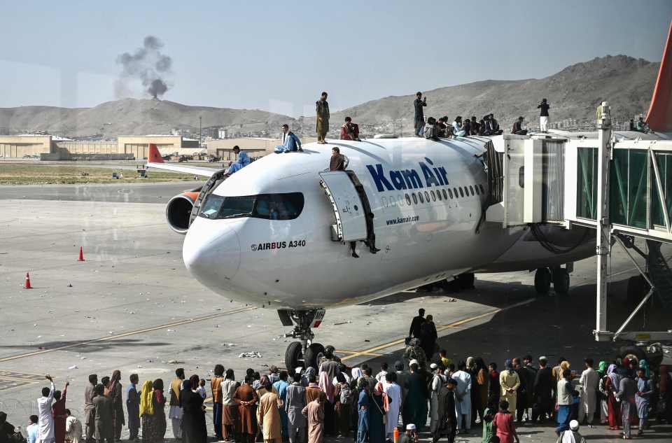 Afghan people climb atop a plane as they wait at the Kabul airport