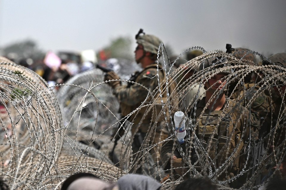 US soldier stand guard behind barbed wire as Afghans gather on a roadside near the military part of the airport