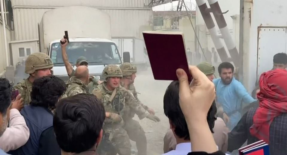 A soldier raises his pistol as people hold up British passports