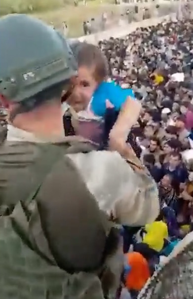 A Turkish soldier guarding the Kabul Airport in Afghanistan picks up an Afghan child from the desperate crowd on the other side of the perimeter wall