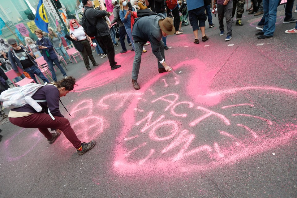 Demonstrators spray paint 'act now' onto the floor