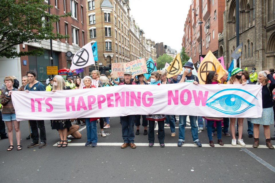 XR marchers carry a banner reading 'it's happening now'