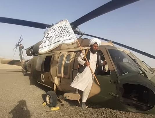 A Taliban fighter holding the group’s flag beside a Black Hawk helcopter