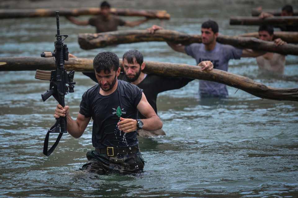 Fighters wade through the water with wooden logs during training