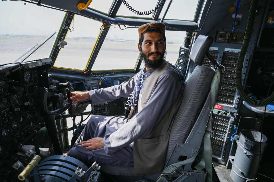 A Taliban fighter poses inside the cockpit of an aircraft left behind by the US military