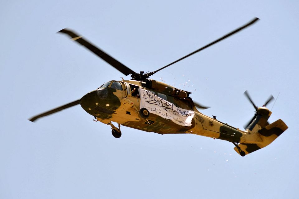 Taliban fighters fly a Black Hawk helicopter with their white flag hanging from the side