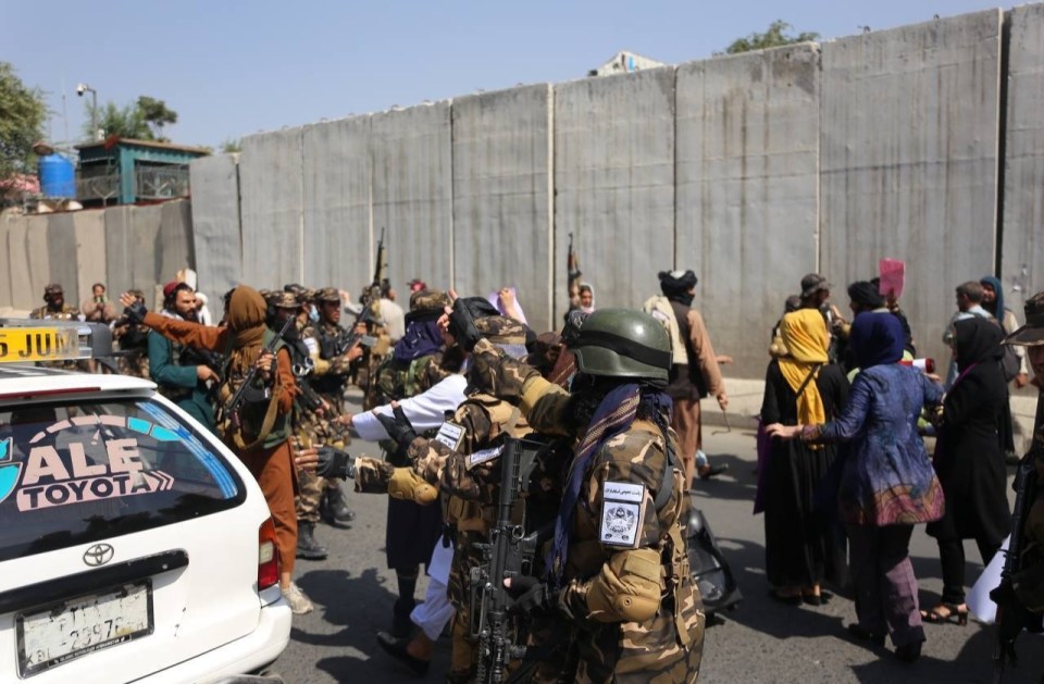 Taliban forces raise their guns as they surround the protesters