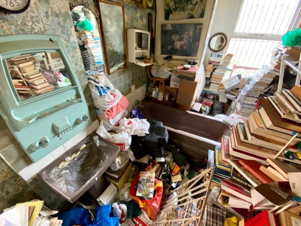 The room is stacked high with piles of books and other clutter