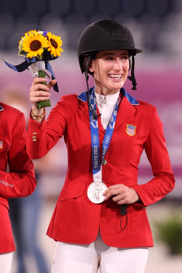 a woman in a red jacket is holding a bouquet of sunflowers and wearing a tokyo 2020 medal around her neck