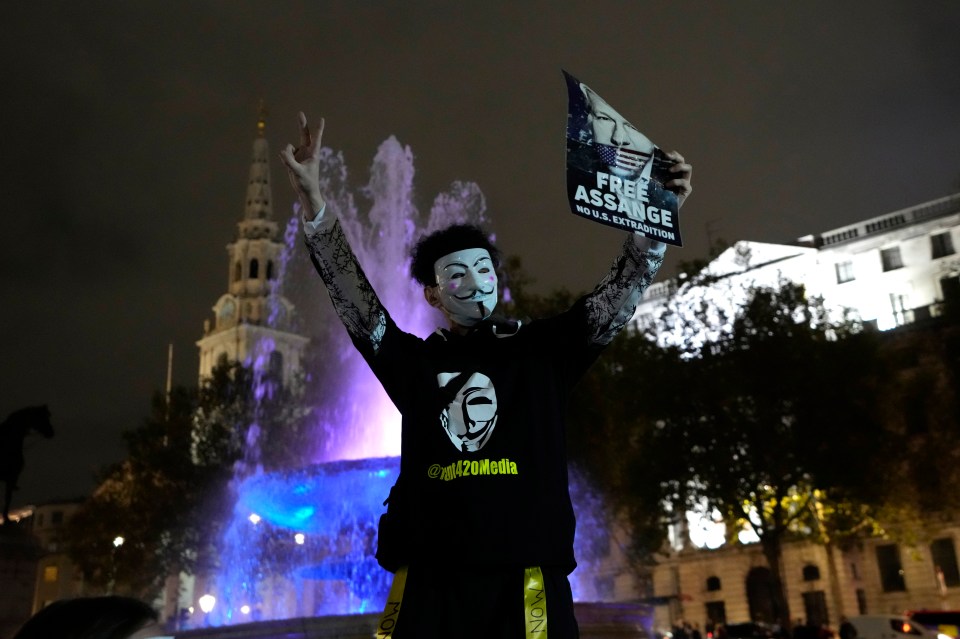 A protester in a Guy Fawkes mask holds a 'Free Assange' poster