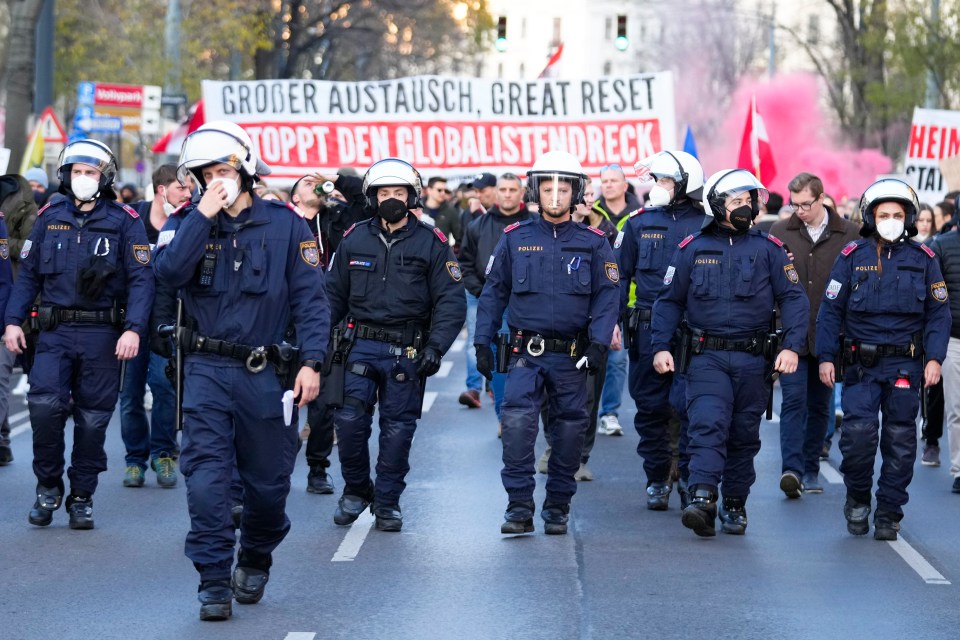 Police officers walk in front of a protest against lockdown in Austria