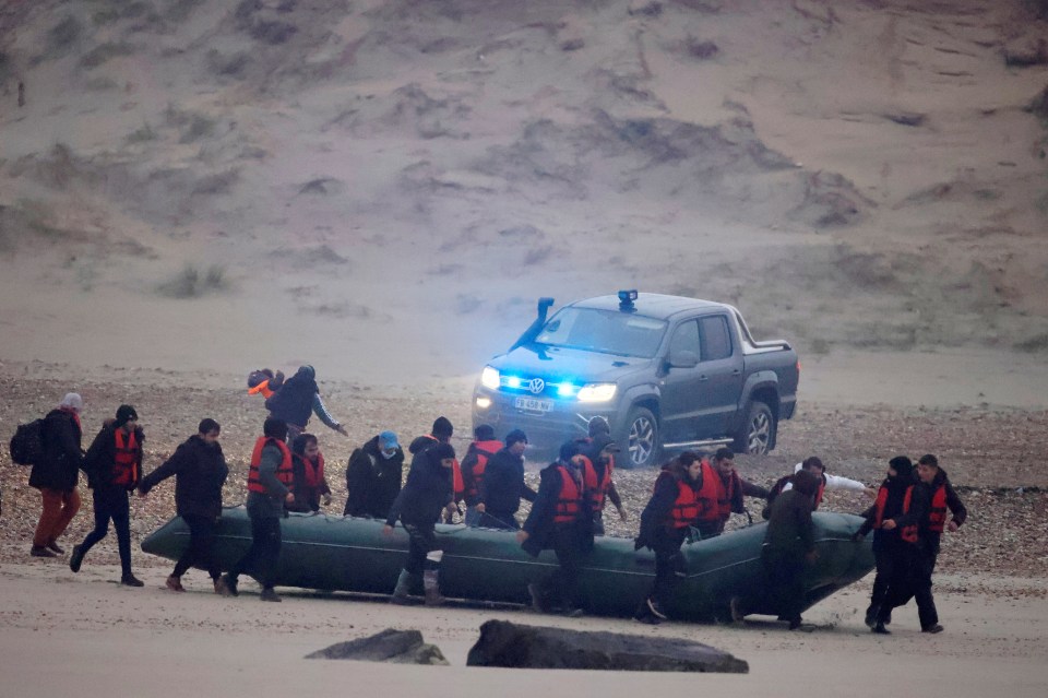 French police watch on as dozens of migrants head to sea in an inflatable dinghy