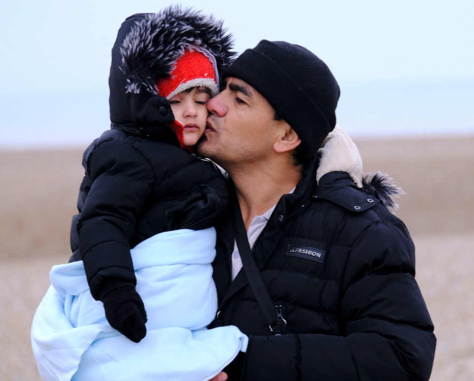 A migrant girl is kissed by her relieved dad after they arrived in the UK, on the same day 27 died