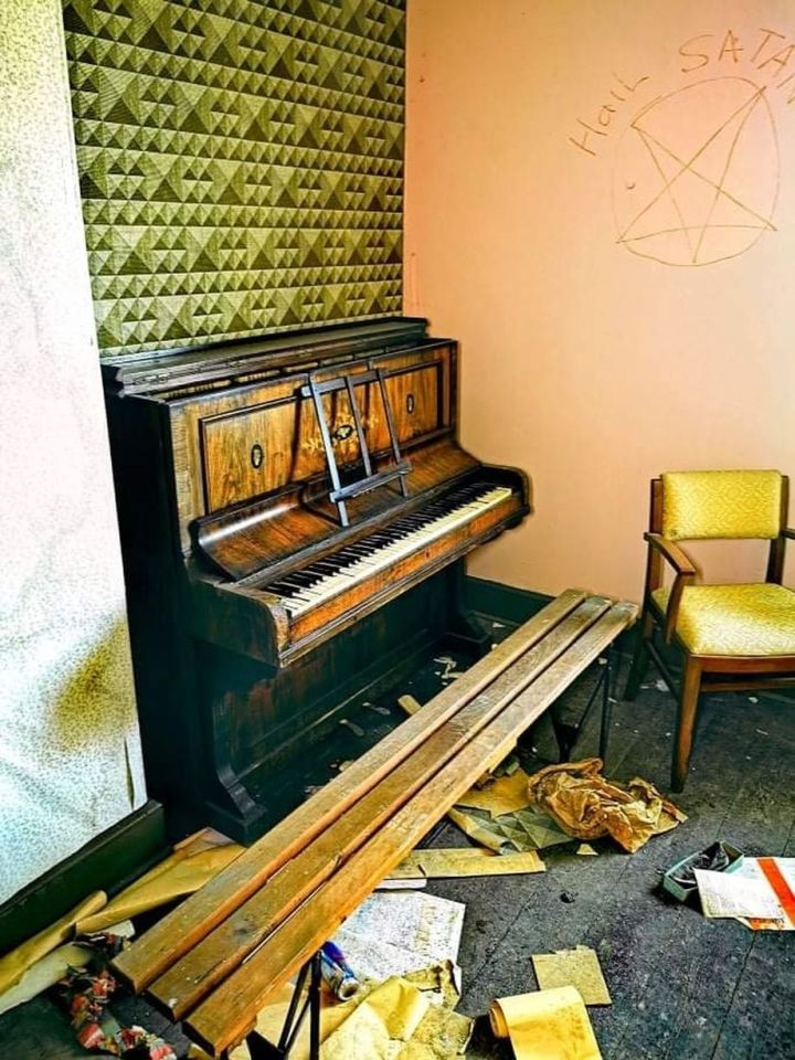 A piano is left untouched as graffiti is scribbled on the wall