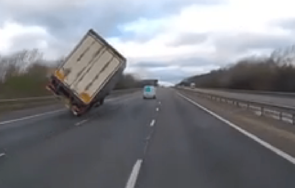 This is the terrifying moment a lorry overturned on a motorway during high winds - narrowly missing a van