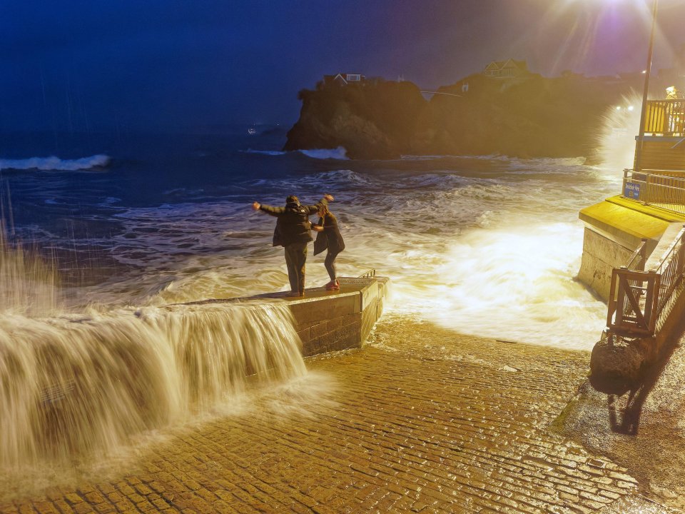 Youngsters stand on a sea wall in Newquay, Cornwall before they are hit by a wave