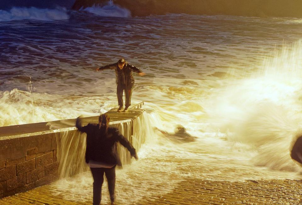 The young woman is swept away from the wall as a young man runs to safety