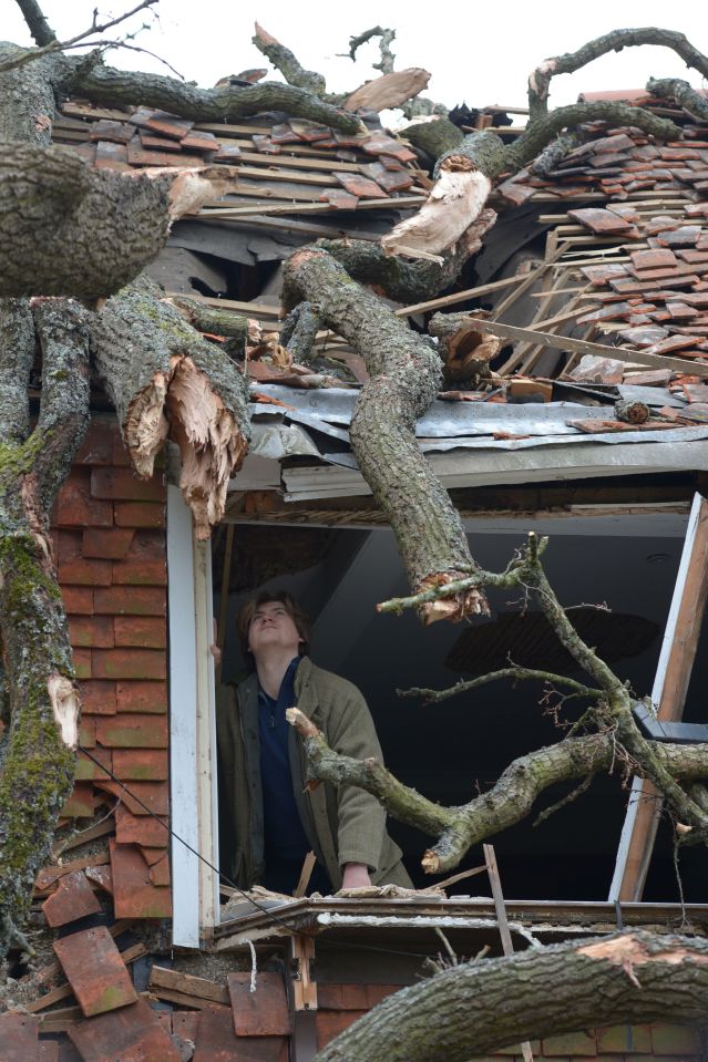 Sven Good, 23, looks out from his bedroom window at the damage caused to the family home in near Brentwood, Essex after a 400-year-old oak fell on Friday