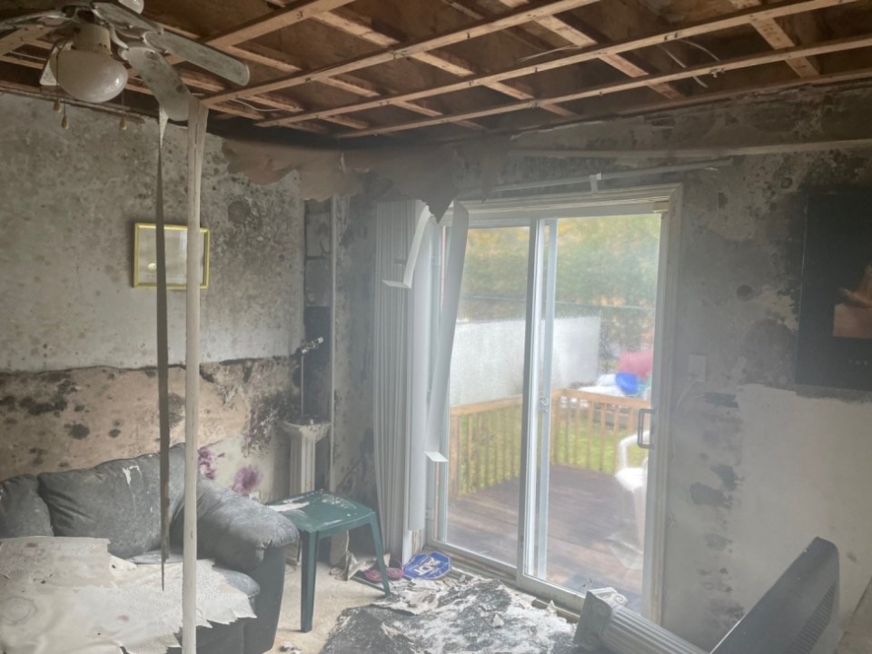 The living room is in a state of disrepair with the wooden beams visible above