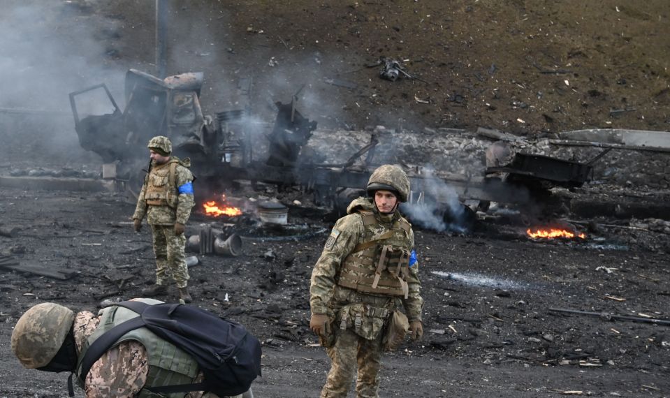 Ukrainian soldiers beside a burning vehicle as fighting continues in Kyiv