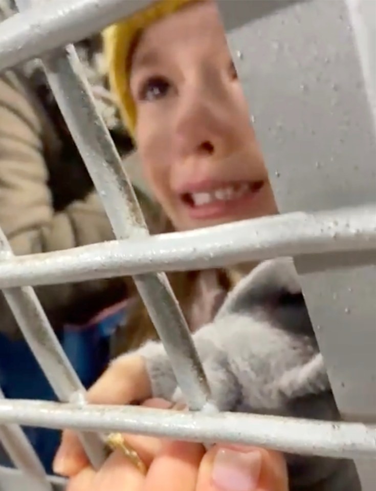 A girl clutches her mother’s hand through the metal grill