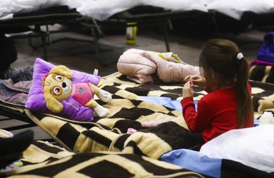 A little girl sits with her Paw Patrol pillow as she takes shelter at a sports hall in  Przemysl, Poland