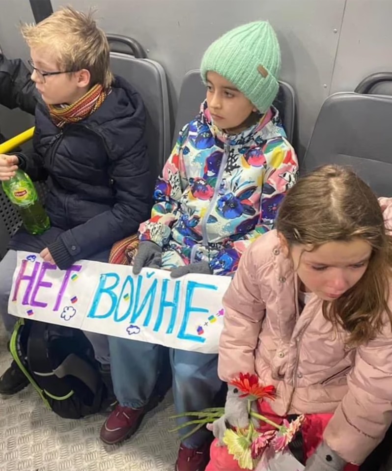 The kids appear to be in the back of a police van, with flowers and a sign saying 'No to war'