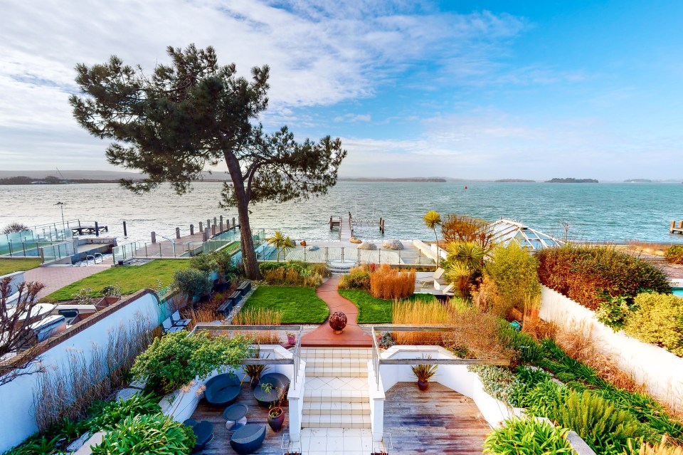 The rear garden has tropical trees and coastal grasses leading to the jetty and boat hoist