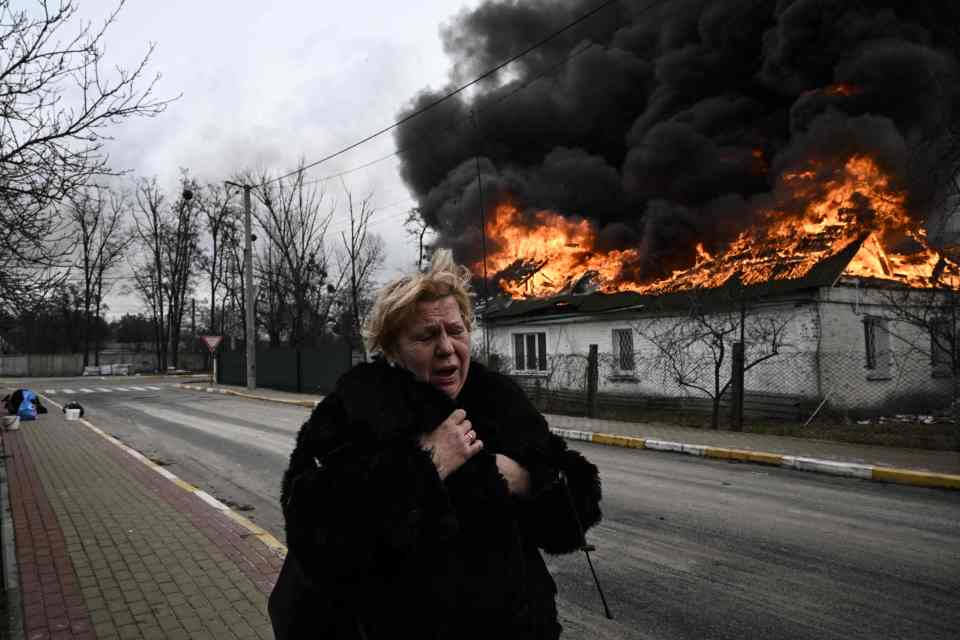 A woman reacts as she stands in front of a house burning after being shelled in the city of Irpin