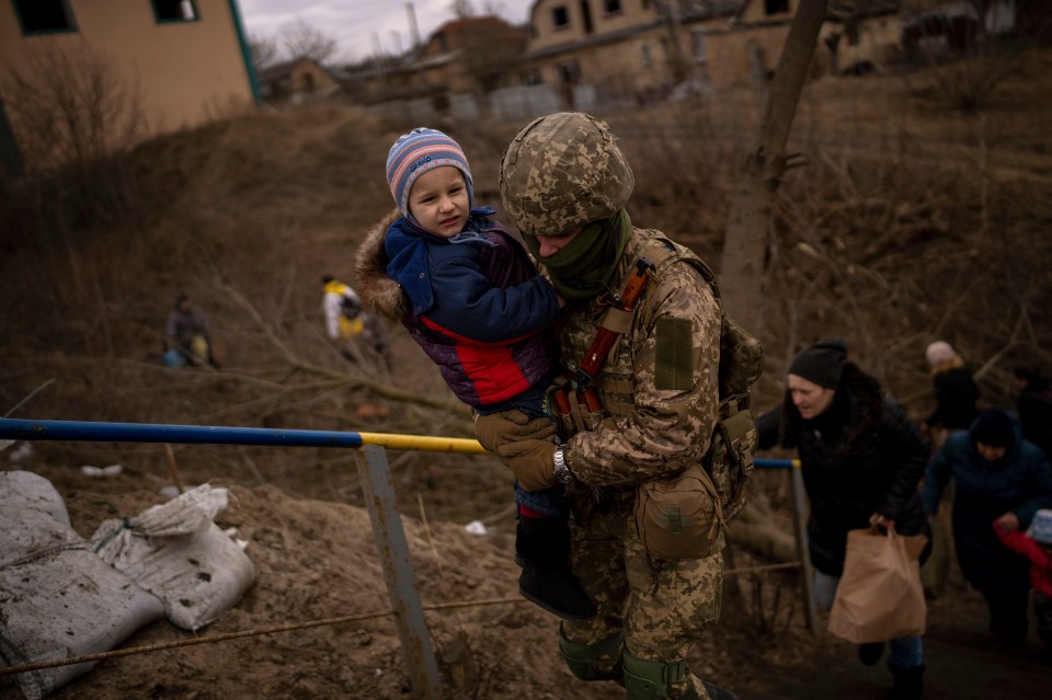 A Ukrainian soldier carries a child as a family flees Irpin