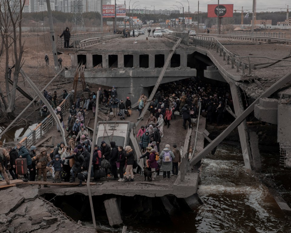 Residents of Irpin cross a destroyed bridge as they try to leave