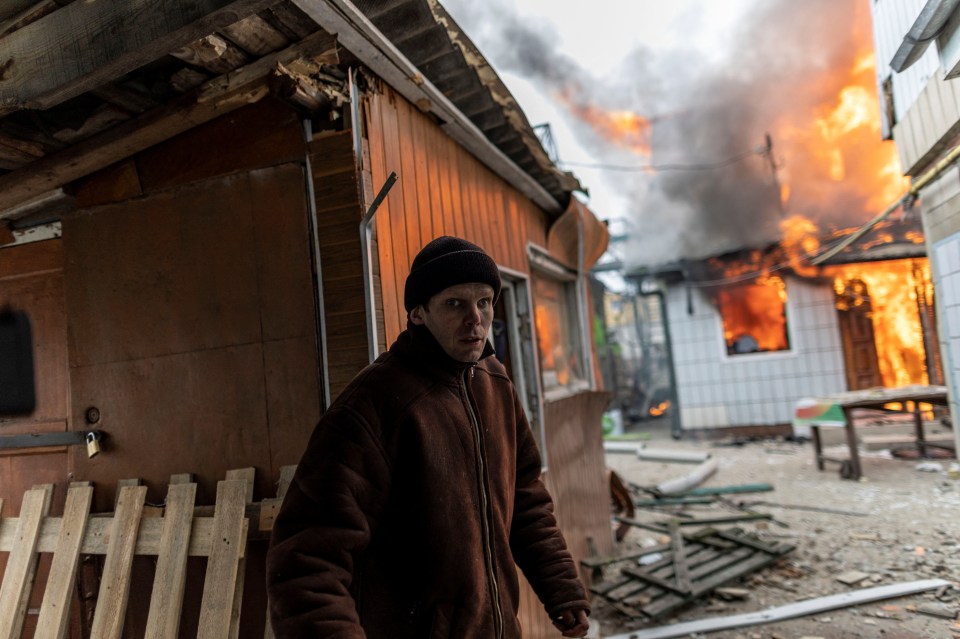 A man walks through Irpin as a nearby house burns