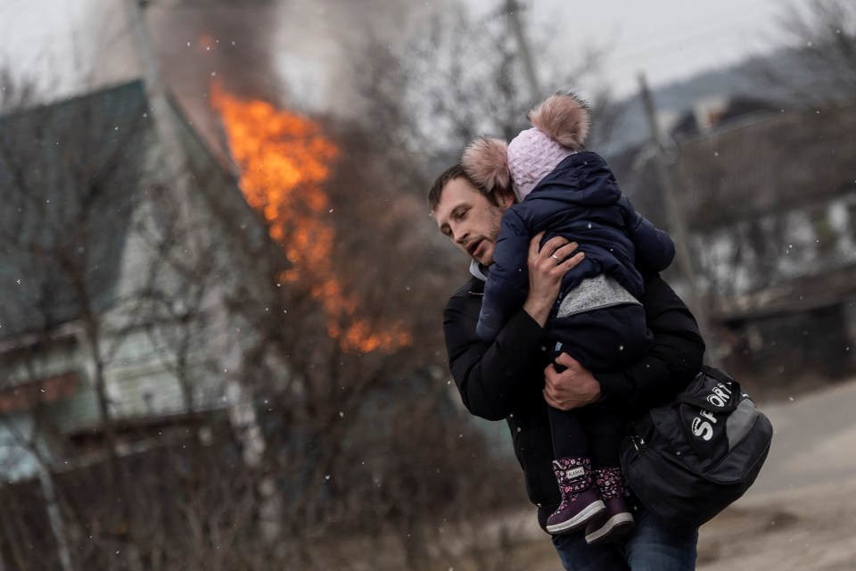 A father carries his daughter in his arms as a fire rages behind them