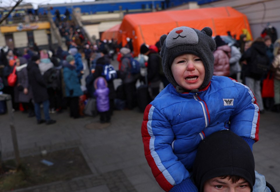 A young boy cries sitting on the shoulders of his brother as they search for their mother outside the train station in Lviv