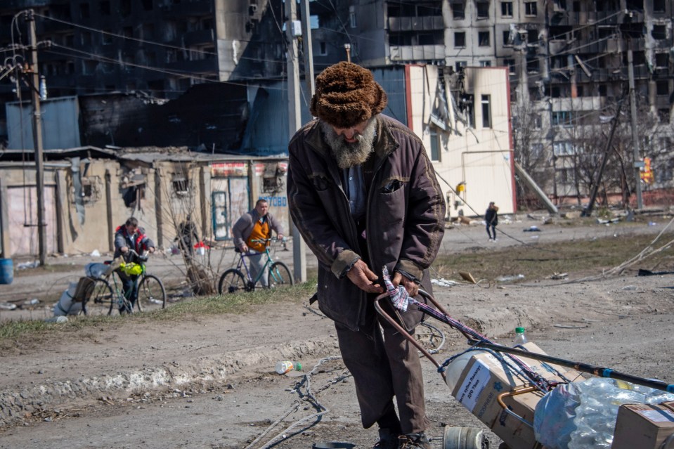 An elderly man carrying his remaining possessions through the street