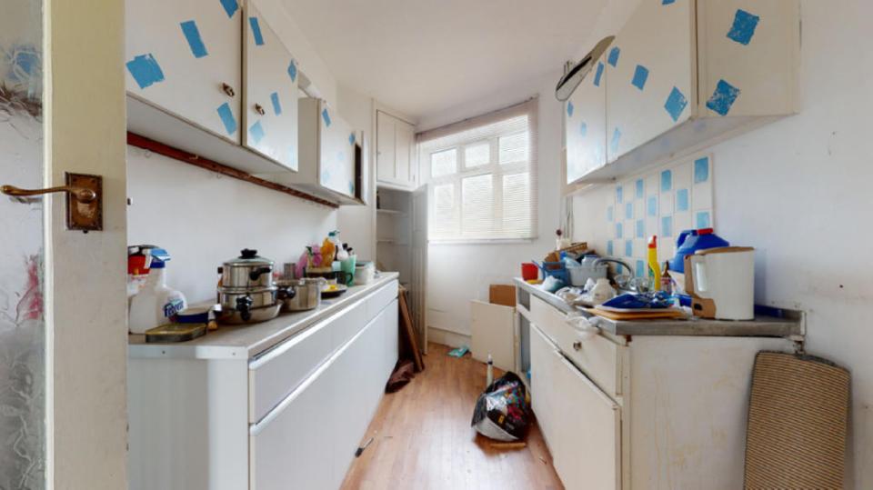 Cluttered kitchen includes pans, plates and mugs on worksurfaces