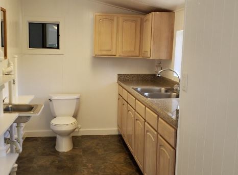 The toilet is located in the middle of the kitchen a few feet from the sink