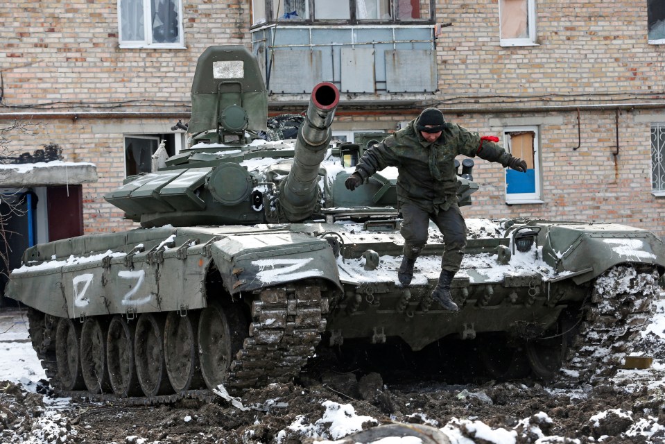 A service member of pro-Russian troops in uniform without insignia jumps off a tank with the letters "Z" painted on it