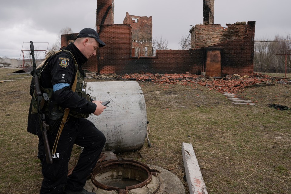 A policeman examines the body of Hennadiy Merchynskyi, 44, who was killed by Russians and dumped in a well in Motyzhyn