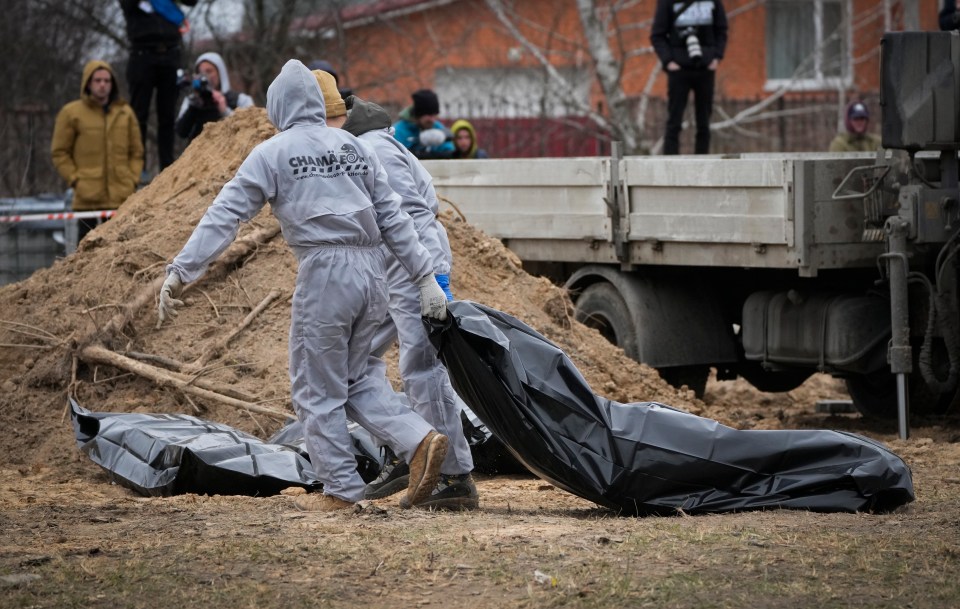 Men wearing protective gear exhume the bodies of civilians killed during the Russian occupation