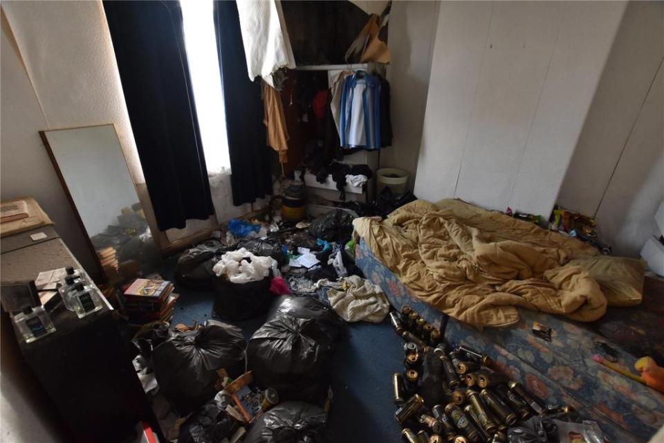 The floor of one of the bedrooms is filled with discarded beer cans and black bin bags