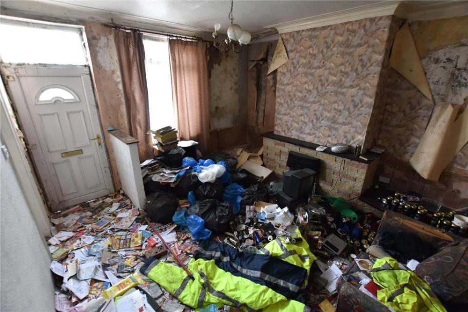 The living room is a complete mess with litter and hi-vis clothing covering the floor