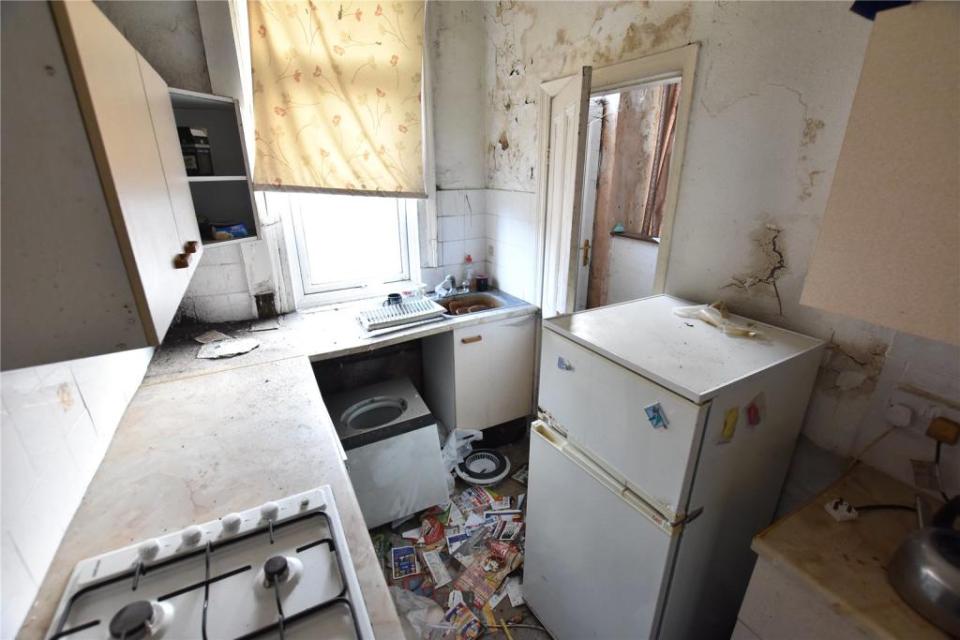 The washing machine in the kitchen has had its door ripped off and huge cracks can be seen in the walls