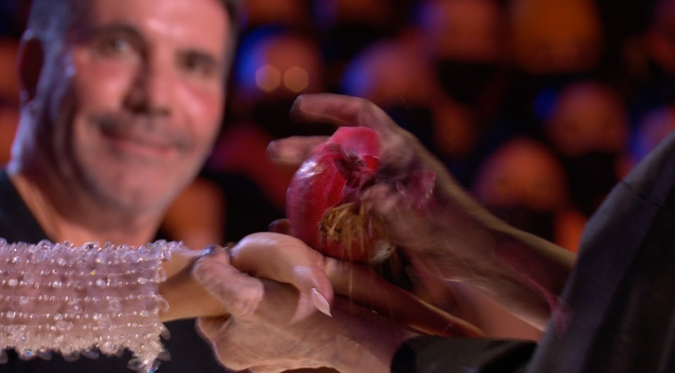 Simon Cowell watches as the performer squeezes an apple onto Amanda Holden's hand