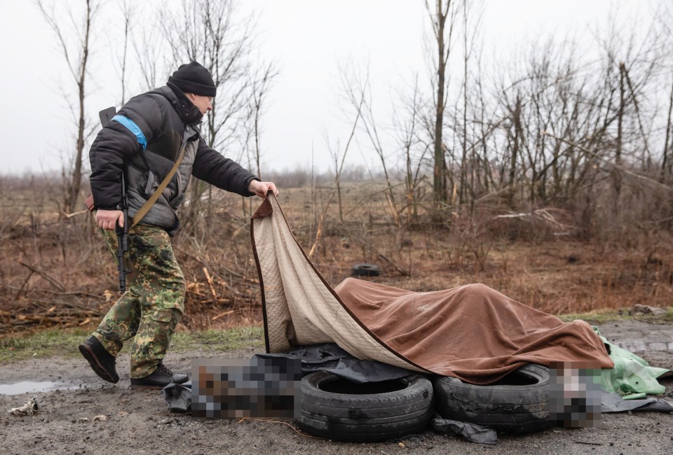 A civilian defence force looks at four dead civilians on the side of a highway under a blanket near Kyiv