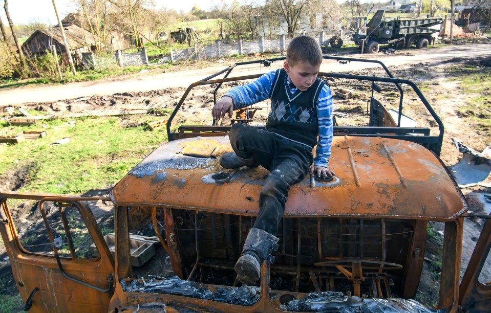 A child perches on a burnt-out military hulk in the liberated Ukrainian village of Lukashivka